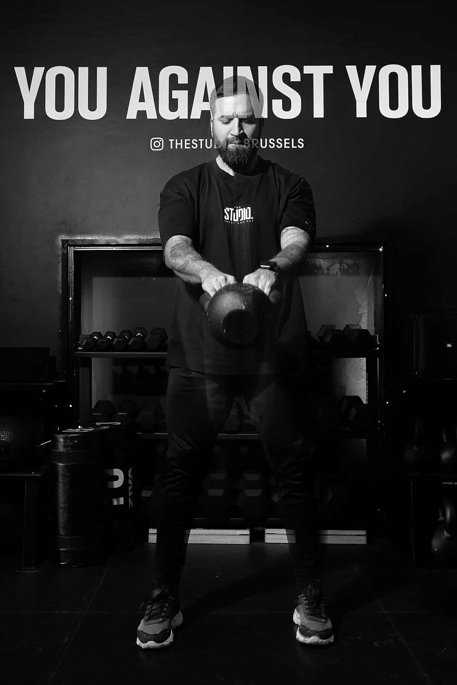 Un coach de The Studio au kettlebell devant le mur « You against you »